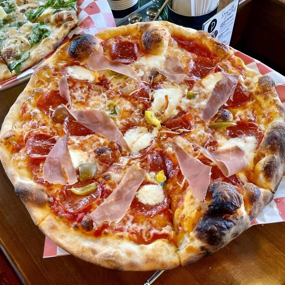 The Parlor's pepperoni and prosciutto pizza with melted cheese and green peppers on a checkered liner.
