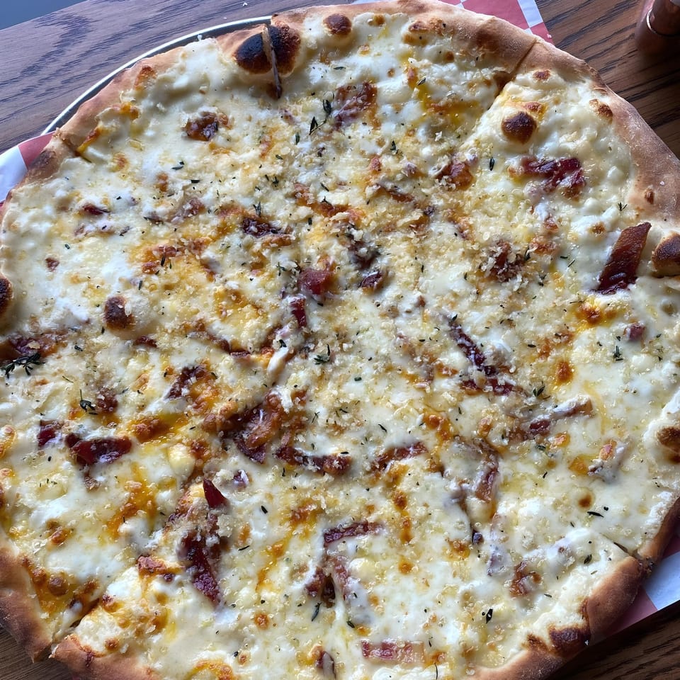 The Parlor's white pizza with bacon, cheese, and herbs on a wooden table.