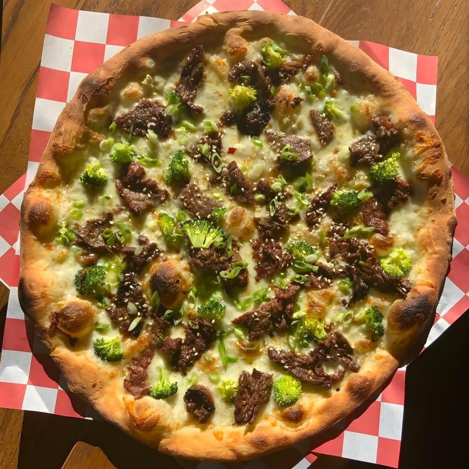 The Parlor's pizza with beef, broccoli, scallions, and sesame seeds on a checkered paper.