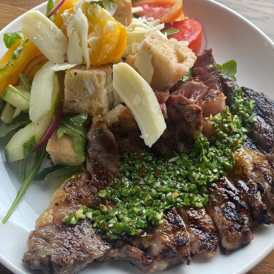Grilled steak with chimichurri sauce, served with a side salad of croutons, cheese, and vegetables.
