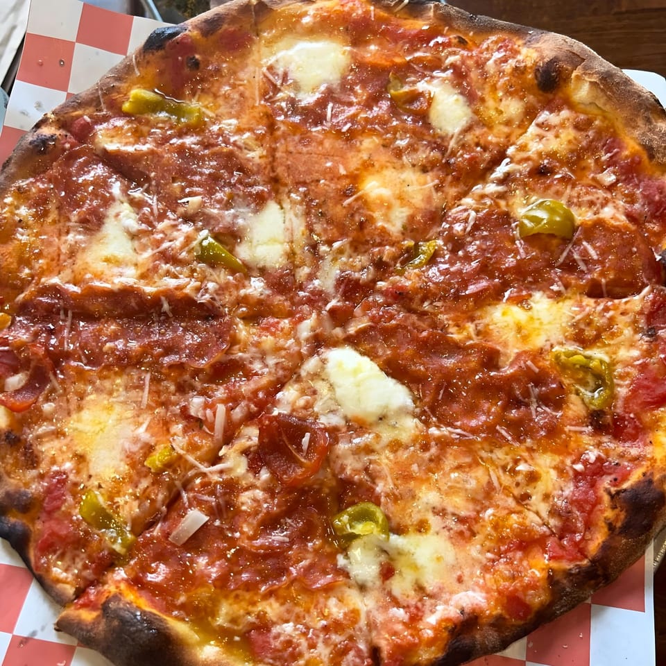 A close-up of a pepperoni and banana pepper pizza from The Parlor, with melted cheese and a crispy crust.