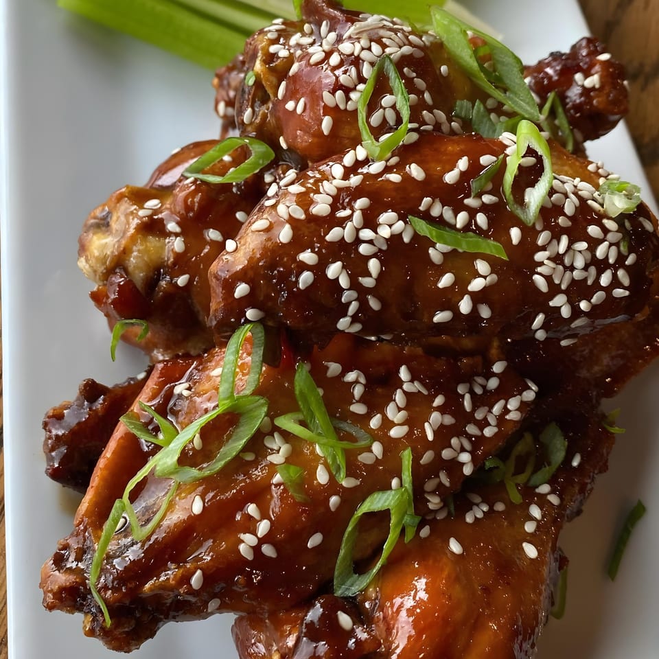 Sweet and spicy chicken wings, glazed with sesame seeds and green onions on a white plate.