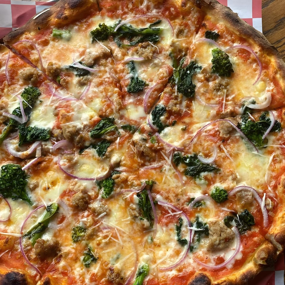 The Parlor's pizza with sausage, broccoli, red onion, and melted cheese, sliced and ready to eat.
